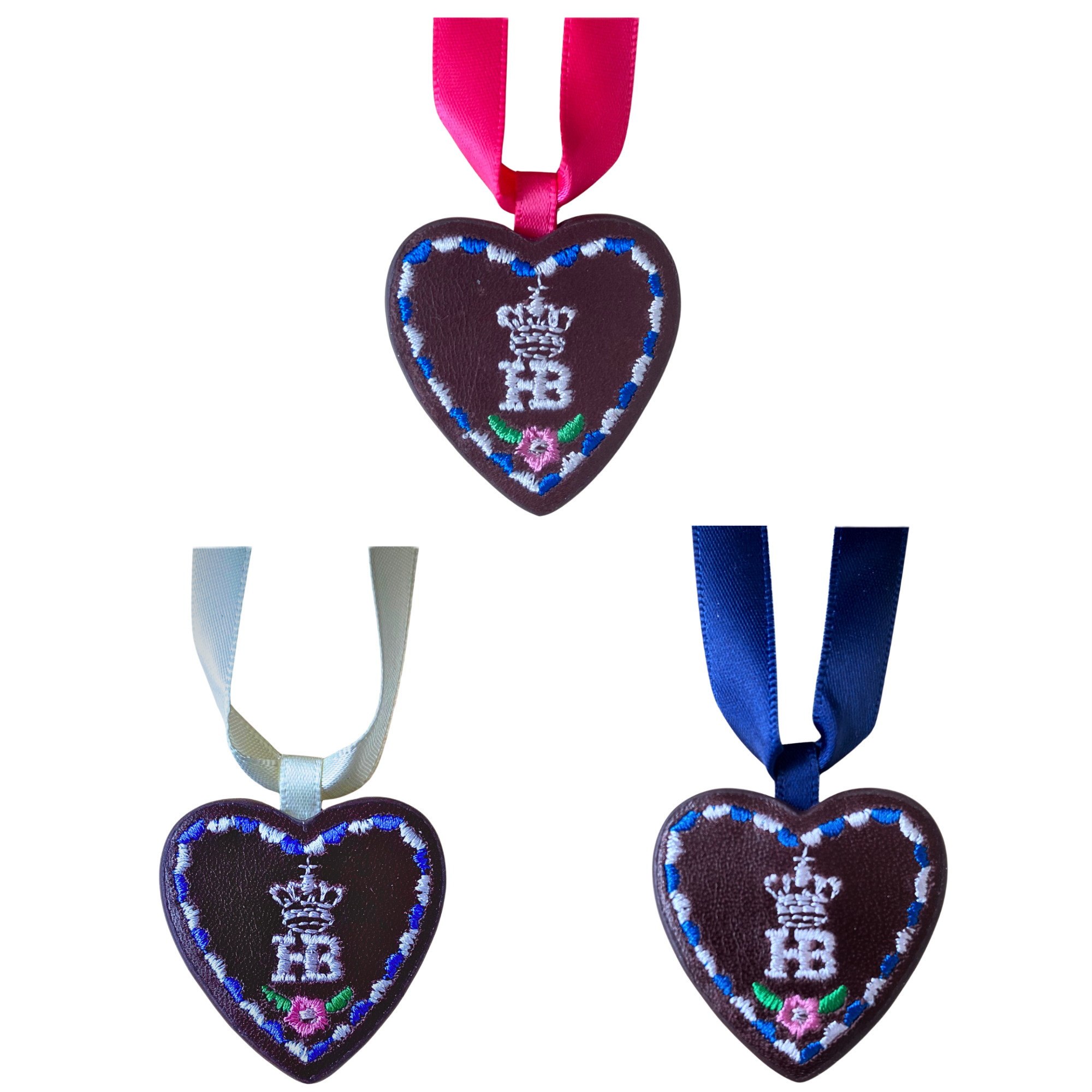 Drei herzförmige Lebkuchen-Anhänger aus Leder mit Hofbräu-Logo und bunten Bändern in Pink, Weiß und Blau.