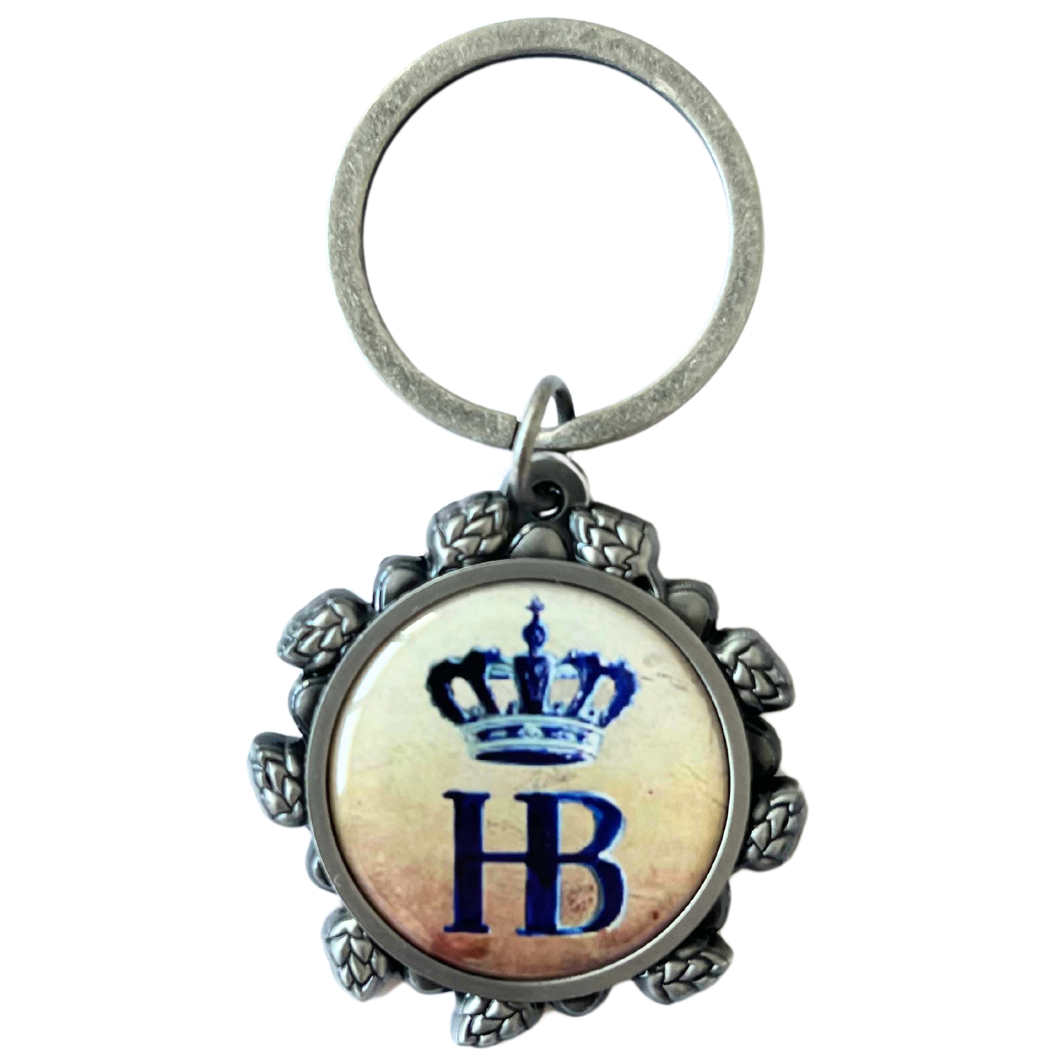 „Schlüsselring mit rundem Medaillon, verziertem Rand und blauem ‚HB‘-Logo mit Krone. Der Rand ist mit Hopfen- und Blattornamenten gestaltet.“