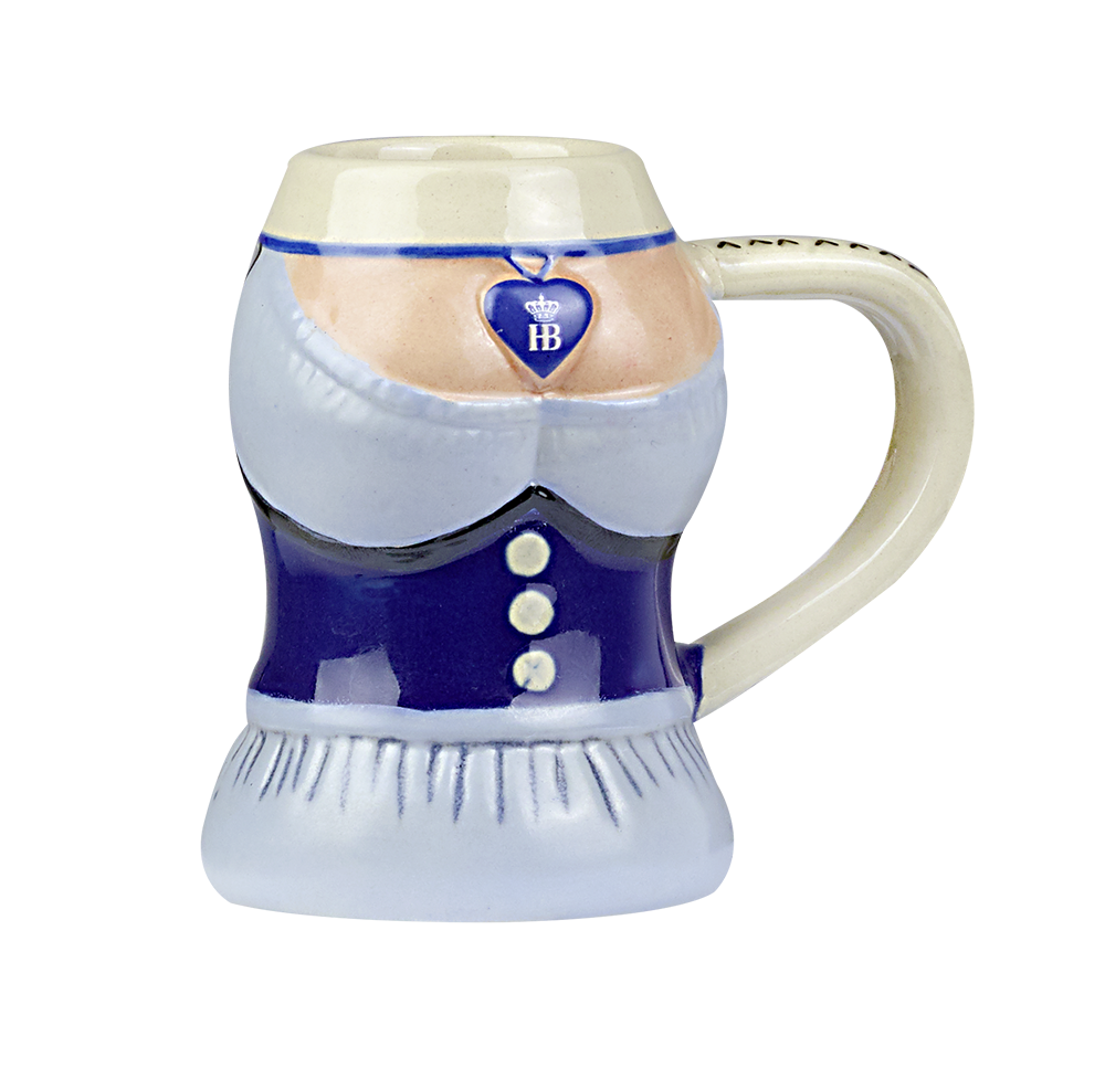 Steingut-Schnapsglas in Form eines Dirndls gestaltet. Das Glas ist bunt bemalt und zeigt ein blaues Mieder mit Knöpfen, eine weiße Bluse und ein Dekolleté. Um den Hals ist ein Herzanhänger mit dem blauen HB-Logo (Hofbräuhaus) und einer Krone zu sehen. Sei
