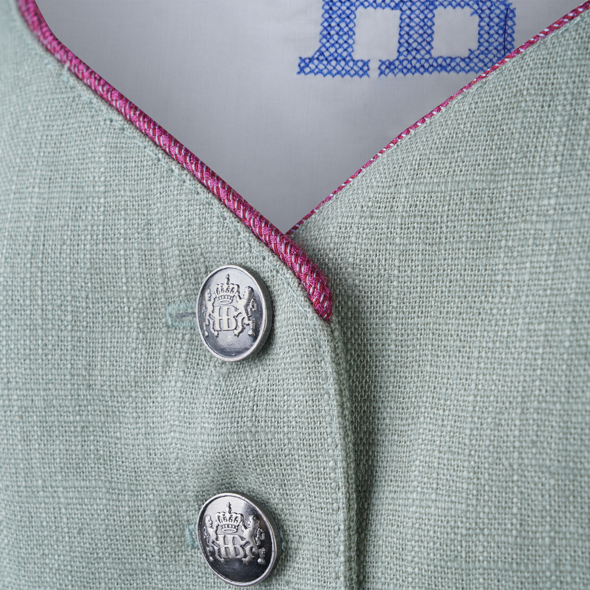 Nahaufnahme des Dirndlausschnitts mit weißem Innenfutter, goldenem Kronenlogo und blauer "HB"-Stickerei, eingefasst mit einer feinen pinken Paspel.