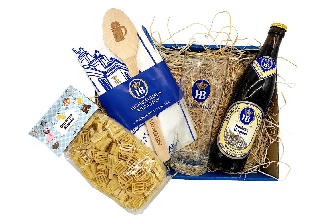 Geschenkset vom Hofbräuhaus München mit einer Flasche Hofbräu Original Bier, einem HB-Bierglas, Nudeln in Bierkrug-Form, einem Geschirrtuch mit Holzkochlöffel – dekorativ verpackt in einer Geschenkbox mit Holzwolle.
